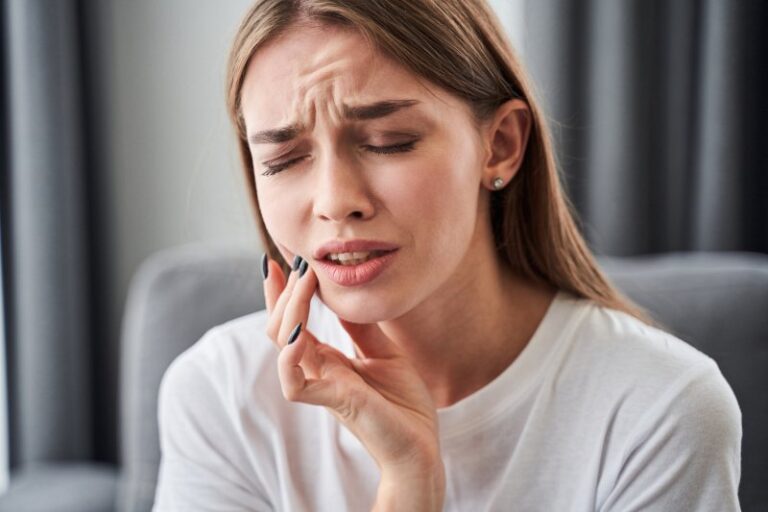 A woman holding her cheek with her hand and grimacing from toothache