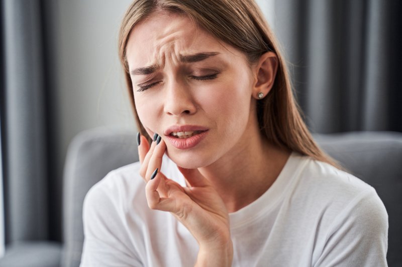 A woman holding her cheek with her hand and grimacing from toothache
