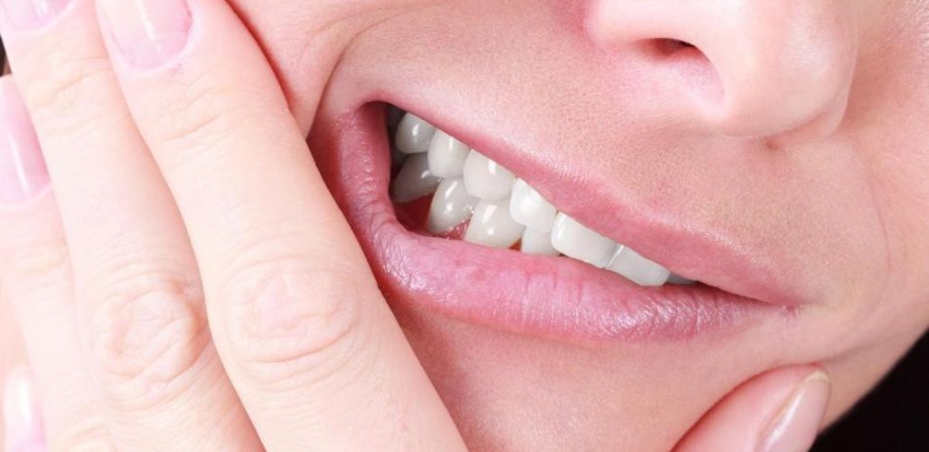 A woman clenching her teeth with her hands held against her jaw, showing the jaw discomfort that teeth grinding can cause