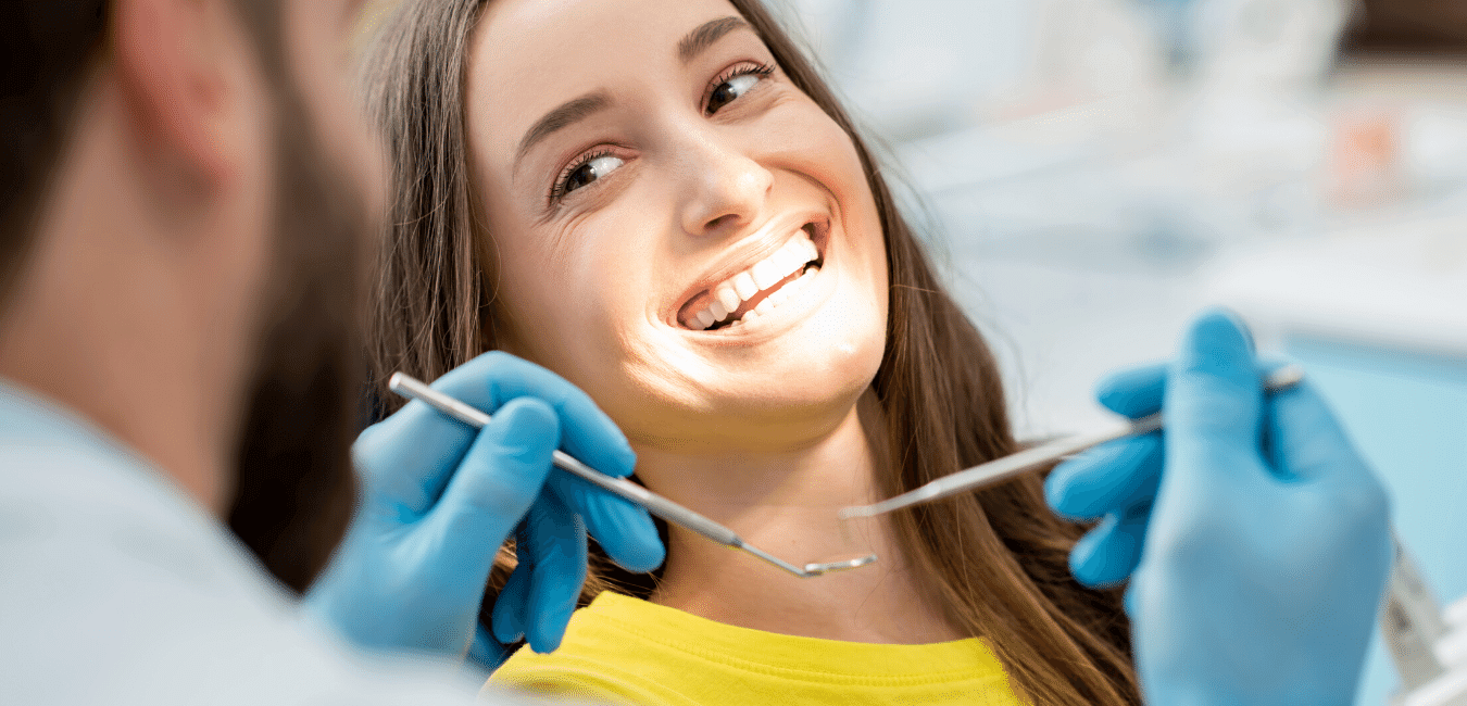 A smiling patient in the dental chair while a dentist examines her teeth with a dental mirror